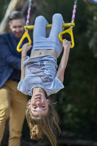 Mädchen hängt am Trapez mit Vater im Hintergrund, lizenzfreies Stockfoto