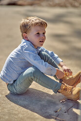 Boy sitting outdoors lacing his boots - BEF00161