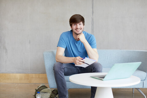 Porträt eines jungen männlichen Studenten, der auf einem Sofa im Studienraum einer Hochschule sitzt, lizenzfreies Stockfoto