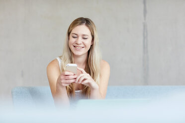 Young female student sitting on study space sofa using smartphone at higher education college - CUF22162