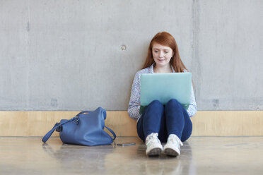 Young female student sitting on floor using laptop at higher education college - CUF22177