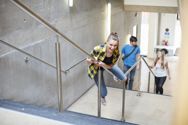 Young female student sliding down stairway handrail at higher education college - CUF22180