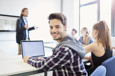 Porträt eines jungen männlichen Studenten, der einen Laptop im Klassenzimmer einer Hochschule benutzt - CUF22188