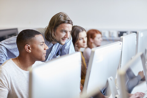 Männlicher Dozent zeigt einem Studenten die Benutzung eines Computers in einem Computerraum einer Hochschule, lizenzfreies Stockfoto