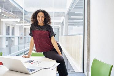 Portrait of young female designer sitting on desk in design studio - CUF22215