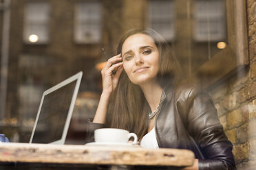Window view portrait of young businesswoman with laptop in cafe - CUF22260