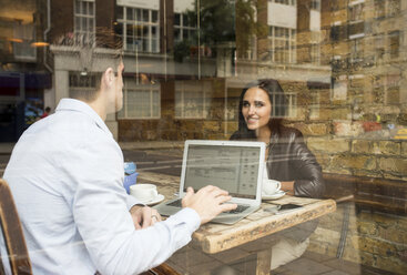 Blick aus dem Fenster auf einen Geschäftsmann und eine Frau, die in einem Café arbeiten, London, UK - CUF22282