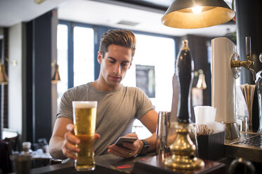 Junger Mann liest Smartphone in einer Bar in der Stadt - CUF22284