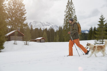 Mid adult man snowshoeing across snowy landscape, dog beside him, Elmau, Bavaria, Germany - CUF22290