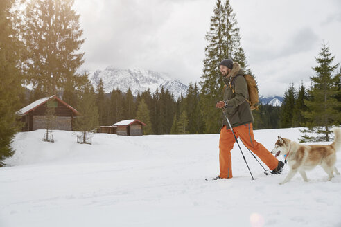 Erwachsener Mann auf Schneeschuhen in verschneiter Landschaft, Hund neben ihm, Elmau, Bayern, Deutschland - CUF22290