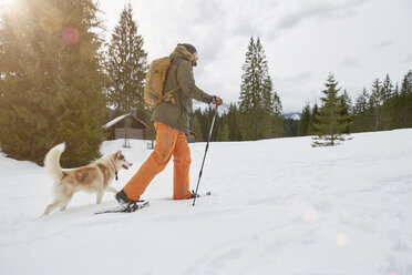 Mid adult man snowshoeing across snowy landscape, dog beside him, Elmau, Bavaria, Germany - CUF22291