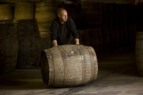 Arbeiter rollt Whiskyfass in Whiskybrennerei, lizenzfreies Stockfoto