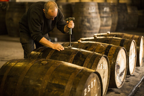 Männlicher Arbeiter beim Öffnen eines hölzernen Whisky-Fasses in einer Whisky-Destillerie - CUF22341