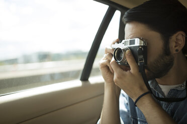 Young man on the road, taking photographs through car window - CUF22355