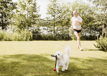 Woman running after coton de tulear dog in garden, Orivesi, Finland - CUF22380