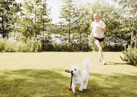 Frau rennt hinter einem Coton de Tulear Hund im Garten her, Orivesi, Finnland - CUF22380