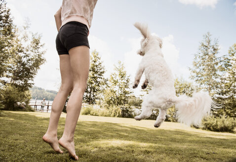 Frau springt mit Coton de Tulear Hund im Garten, Orivesi, Finnland - CUF22383