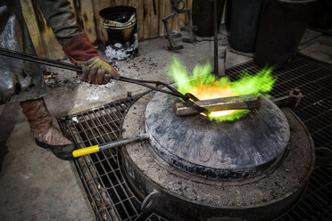 Männlicher Gießereiarbeiter beim Erhitzen eines Bronzeblocks über einem Ofen in einer Bronzegießerei - CUF22418