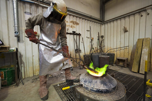 Männlicher Gießereiarbeiter beim Erhitzen eines Bronzeblocks über einem Ofen in einer Bronzegießerei - CUF22419
