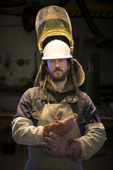 Porträt eines erwachsenen männlichen Gießereiarbeiters, der in einer Bronzegießerei Schutzhandschuhe anzieht - CUF22423