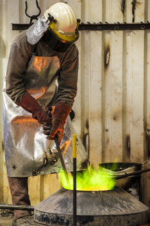 Männlicher Gießer bei der Arbeit mit einem grün befeuerten Ofen in einer Bronzegießerei - CUF22425