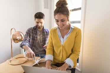 Moving house: Young man unpacking box, young woman using laptop - ISF07910