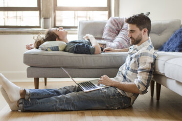 Junges Paar entspannt sich zu Hause, junge Frau schläft auf Sofa, junger Mann benutzt Laptop - ISF07915