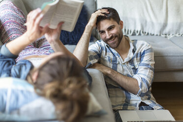 Young couple relaxing at home, young woman lying on sofa, young man sitting on floor, laughing - ISF07916