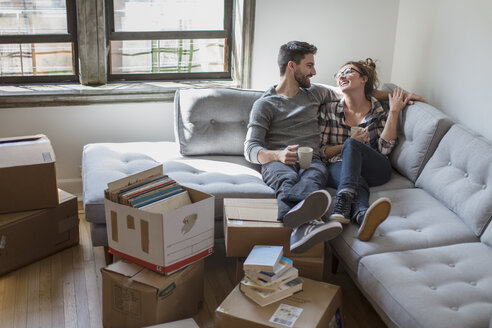 Moving house: Young couple relaxing on sofa surrounded by cardboard boxes - ISF07917