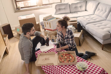 Moving house: Young couple eat pizza in new home, surrounded by boxes - ISF07920