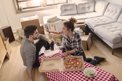 Umzug: Junges Paar isst Pizza im neuen Haus, umgeben von Kartons - ISF07920