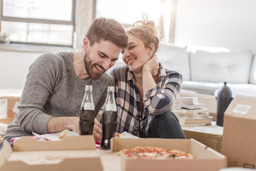 Umzug: Junges Paar isst Pizza im neuen Haus, umgeben von Kisten - ISF07921