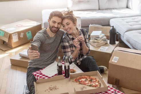 Umzug: Junges Paar nimmt Selbstporträt mit Smartphone auf, im neuen Haus, umgeben von Kisten - ISF07922