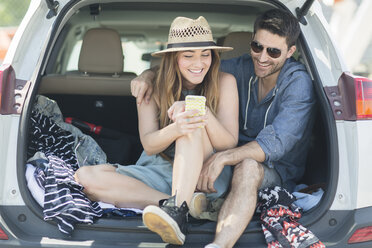 Couple in car boot looking at smartphone - ISF07936