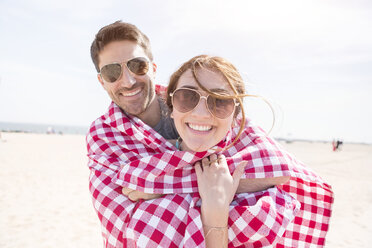 In eine Picknickdecke eingewickeltes Paar schaut lächelnd in die Kamera, Coney Island, Brooklyn, New York, USA - ISF07955