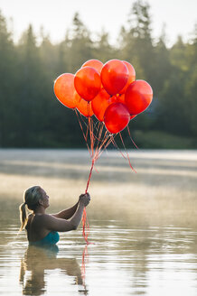 Frau im Wasser, die ein Bündel roter Luftballons hält - ISF07979