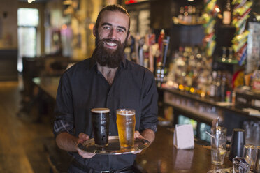 Porträt eines jungen männlichen Barkeepers, der ein Tablett mit Bier in einem Gasthaus trägt - ISF08050