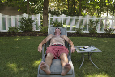 Senior man sunbathing on garden sun lounger listening to earphones - ISF08060