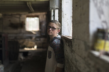 Porträt eines Teenagers mit getönter Brille, der an einer Schuppenwand lehnt - ISF08063