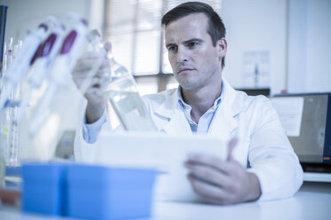 Mid adult man in laboratory, reading label of bottle - ISF08096