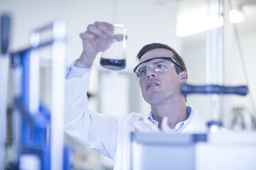 Mittlerer erwachsener Mann im Labor, der eine Flüssigkeit in einem Glaskolben betrachtet - ISF08100