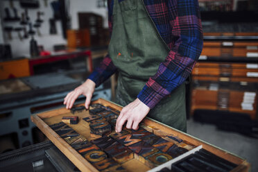 Crop of young craftsman looking through tray of wooden letterpress letters in print workshop - CUF22515