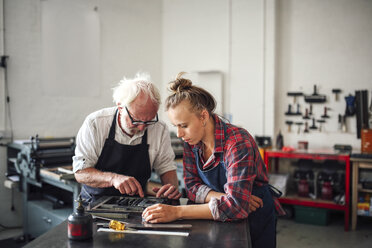 Ein älterer Handwerker arbeitet mit einer jungen Handwerkerin in der Druckwerkstatt am Buchdruck - CUF22527