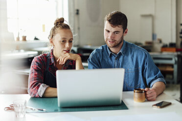 Young craftsman and craftswoman looking at laptop in print studio workshop - CUF22544