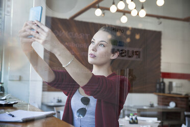Junge Frau sitzt in einem Café, macht ein Selfie und benutzt ein Smartphone - CUF22607
