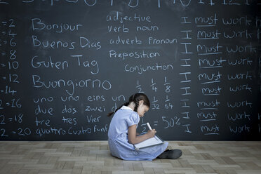 Schoolgirl sitting studying in front of large chalkboard with schoolwork chalked on it - CUF22628
