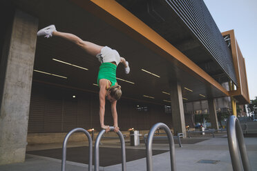 Junge Frau macht Handstand auf Metallstange in städtischer Umgebung - ISF08263