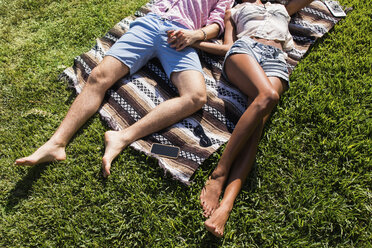 Young couple relaxing outdoors, lying on blanket on grass, holding hands, low section - ISF08307