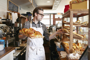 Männlicher Arbeiter in einer Bäckerei, der frisches Gebäck in die Vitrine legt - ISF08380