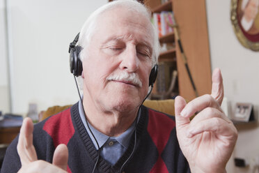 Senior man listening to music on earphones at home - ISF08396